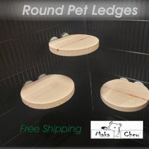 May include: Three round, light-colored wooden pet ledges are mounted inside a black wire cage. The text "Round Pet Ledges" is at the top. The ledges are designed to accessorize a pet's cage.