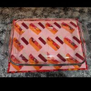 May include: A clear glass baking dish with a pink and orange patterned fabric underneath. The fabric has a geometric design with stripes and squares.