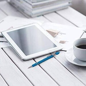 May include: A white tablet computer with a black screen, a blue pen, and a white coffee cup with black coffee on a white wooden table.