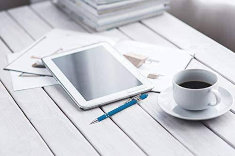 May include: A white tablet computer with a black screen, a blue pen, and a white coffee cup with black coffee on a white wooden table.