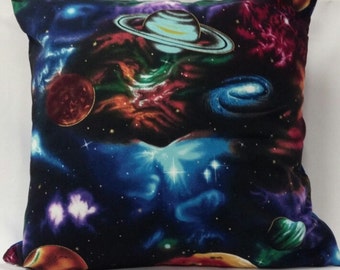 May include: A square throw pillow featuring a vibrant space-themed print on a black background. The design displays colorful nebulae in shades of blue, purple, and red, along with various planets, including one with prominent rings, and a spiral galaxy.
