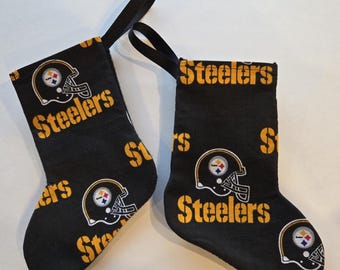 May include: Two black Christmas stockings with a repeating pattern of yellow Steelers football helmets and the word "Steelers". Each stocking has a black loop for hanging.