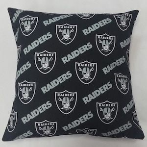 May include: Black and silver pillow with a repeating pattern of the Las Vegas Raiders logo and the word "RAIDERS".
