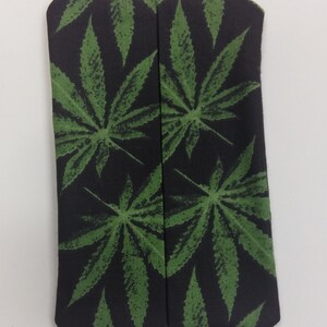 May include: A black fabric pouch with a green marijuana leaf pattern. The pouch is folded in half and has a seam down the center.