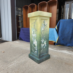 May include: A green pedestal with a painted design of vines and grapes. The pedestal has a square base and a square top.