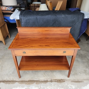 May include: A wooden table with a single drawer and a lower shelf. The table has a rich brown finish and brass hardware.