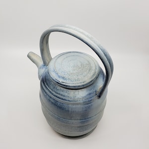 May include: A blue and white ceramic teapot with a lid and a handle. The teapot has a speckled glaze and a slightly textured surface.