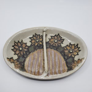 May include: A white ceramic divided serving dish with a floral design and a divider in the center. The dish has a brown and tan floral pattern around the edge and a striped design in the center.