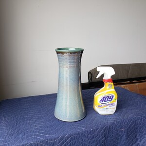 May include: A light blue ceramic vase with a brown rim sits on a blue quilted surface next to a yellow and white spray bottle labeled "409 Multi-Surface Cleaner".