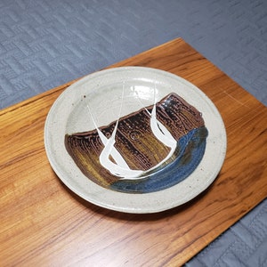 May include: A ceramic plate with a white, brown, and blue glaze design. The plate has a slightly raised rim and a smooth surface.
