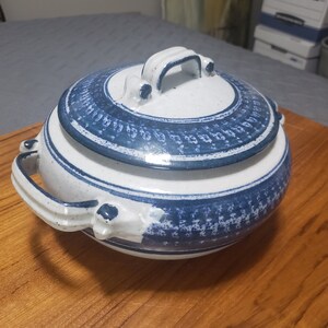May include: A white ceramic serving dish with a blue and white patterned design. The dish has a lid with a handle and two handles on the sides.
