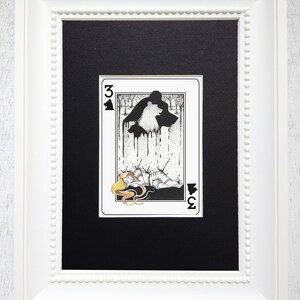 Pu&ograve; includere: Un'illustrazione incorniciata di una carta da gioco, il tre di picche. La carta rappresenta una donna sdraiata a terra con una sagoma di orso sopra di lei. L'orso cola un liquido nero.