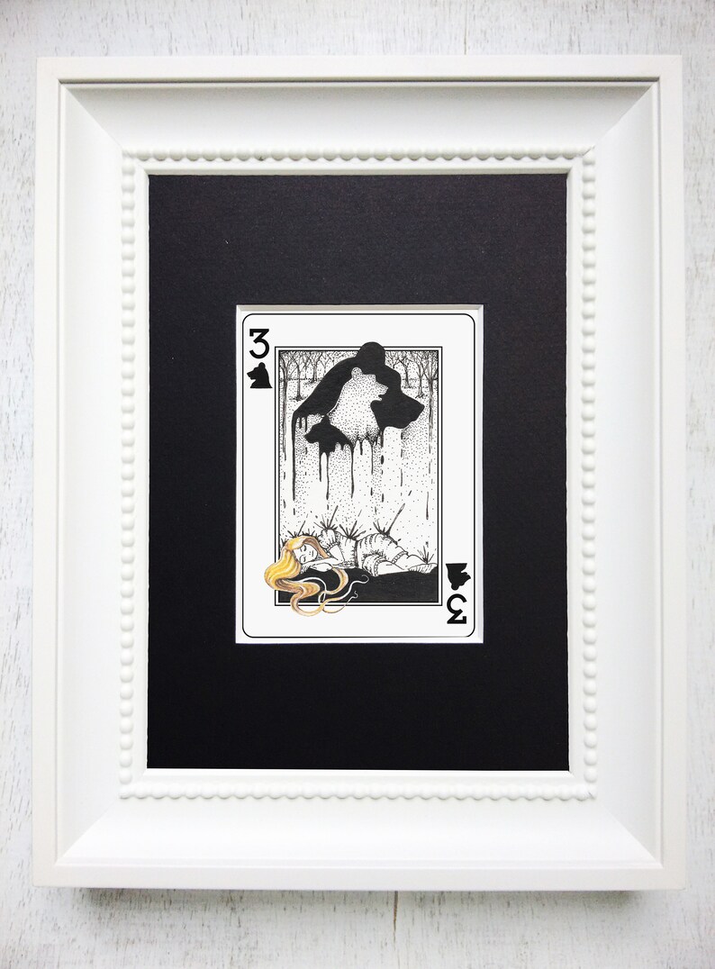 Pu&ograve; includere: Un'illustrazione incorniciata di una carta da gioco, il tre di picche. La carta rappresenta una donna sdraiata a terra con una sagoma di orso sopra di lei. L'orso cola un liquido nero.