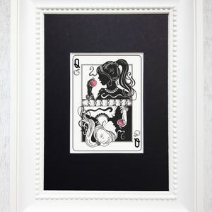 May include: A framed black and white illustration of a queen of hearts playing card. The queen is depicted as a silhouette with a red apple in her hand. The card is framed in a white frame with a beaded border.