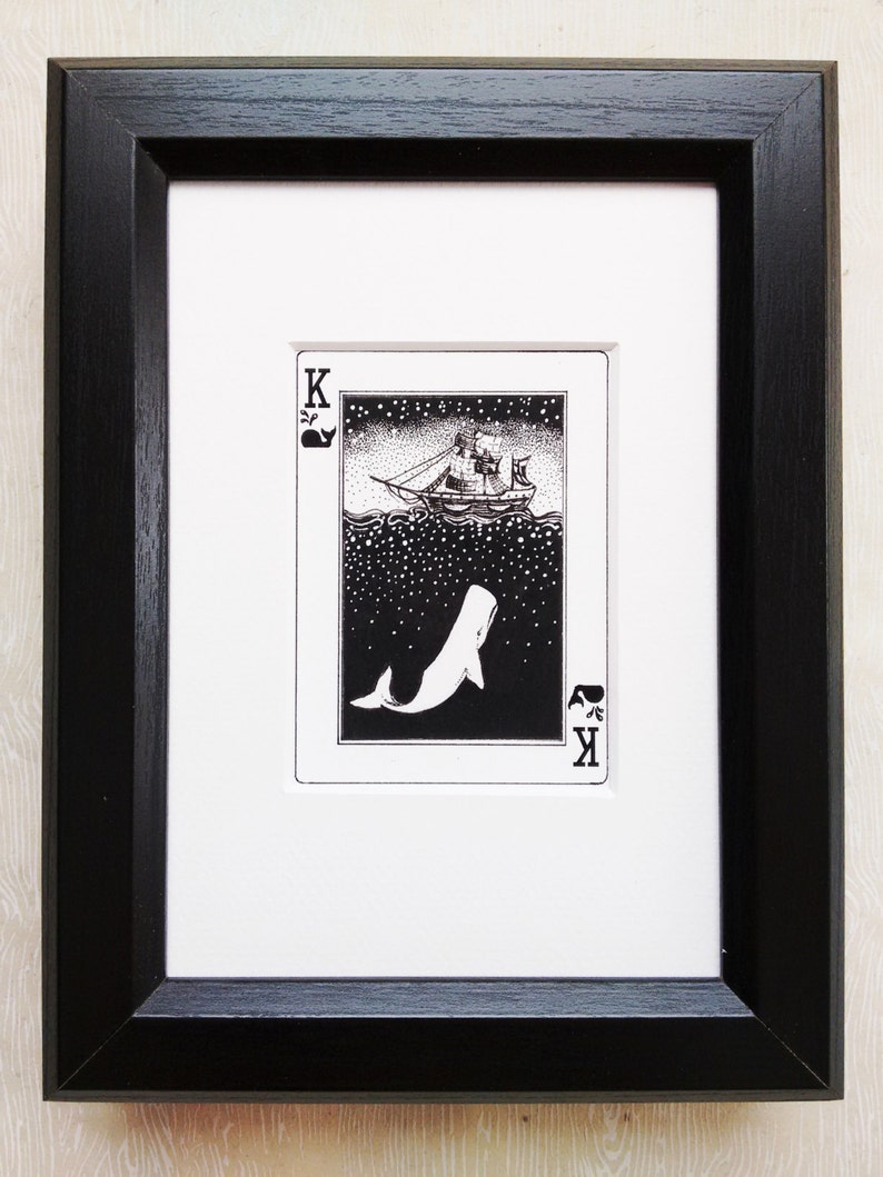 May include: A black and white illustration of a ship sailing on a starry sea with a whale jumping out of the water. The illustration is framed in a black frame and is part of a playing card deck. The card is the King of Spades.