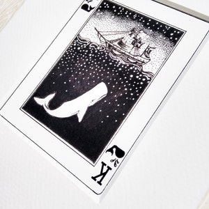 May include: A black and white illustration of a whale and a ship on a playing card. The card is a King of Spades and features a stylised whale with a ship sailing above it. The background is a starry night sky.
