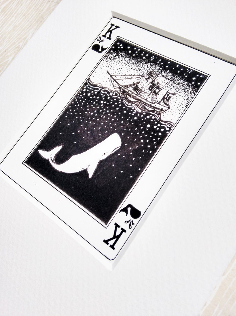 May include: A black and white illustration of a whale and a ship on a playing card. The card is a King of Spades and features a stylised whale with a ship sailing above it. The background is a starry night sky.