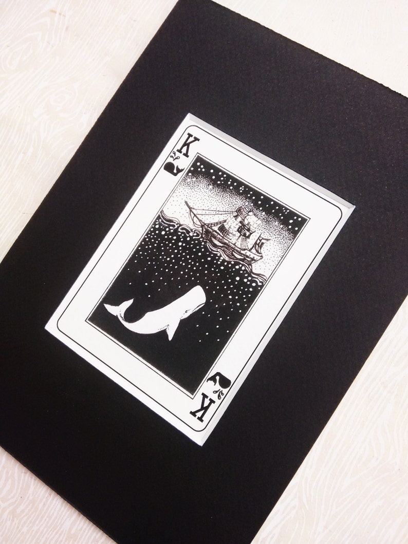 May include: A black and white illustration of a whale leaping out of the water with a ship sailing in the background. The illustration is on a playing card with the letter "K" and a spade symbol in the corner.