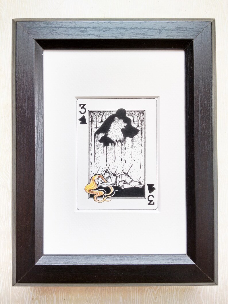 Pu&ograve; includere: Un'illustrazione in bianco e nero di una carta da gioco, il tre di fiori. La carta rappresenta una donna sdraiata con una creatura simile a un lupo sopra di lei. Il lupo sta gocciolando un liquido nero.
