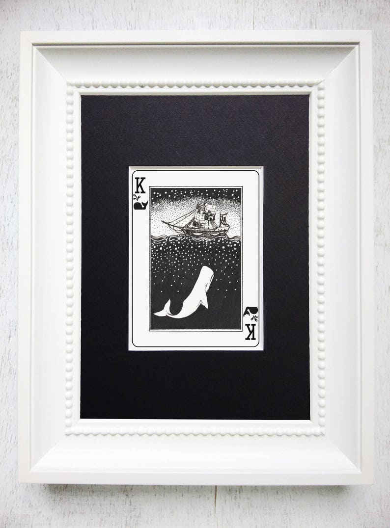 May include: A black and white illustration of a playing card depicting a whale and a ship. The card is a King of Spades and has a black background with white stars. The whale is swimming upwards towards the ship, which is sailing on the surface of the water.