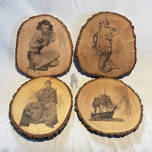 May include: Four wooden round slices with different images burned into the surface. The images are a woman in a swimsuit holding a megaphone, a mermaid, a man in a long coat holding a sword, and a ship with sails.