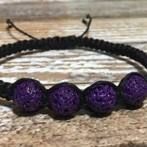 Può includere: Un braccialetto intrecciato nero con cinque perline di lava vulcanica viola.
