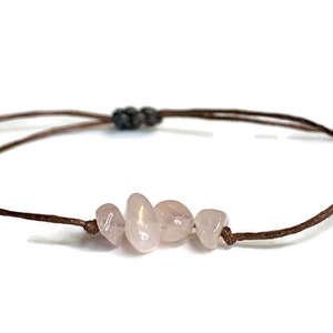 May include: A brown string bracelet with four light pink rose quartz stones.