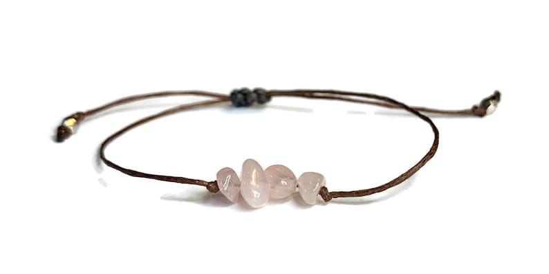May include: A brown string bracelet with four light pink rose quartz stones.