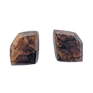 May include: Two matching, geometric-shaped earrings. Each earring features a dark brown, wood-grain pattern encased in a clear, glossy resin. The earrings have a unique, angular design.