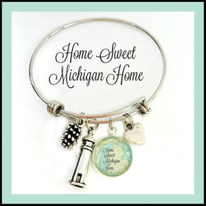 May include: A silver expandable bracelet with charms, including a lighthouse, a pine cone, a heart, and a round charm with a map of Michigan and the text "Home Sweet Michigan Home".