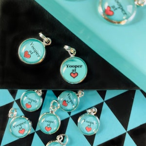 Peut inclure: Un ensemble de breloques en argent avec un fond turquoise et le texte "Yooper at" et un cœur rouge.