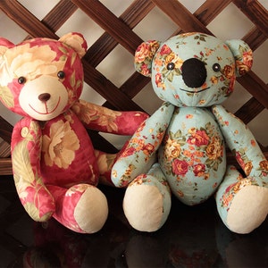 Può includere: Due orsacchiotti di peluche con tessuto floreale. Un orso è rosso con fiori bianchi e gialli, l'altro è blu con fiori arancioni e gialli.