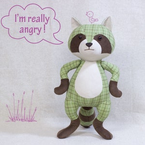 Puede incluir: Un juguete de peluche de mapache verde y marr&oacute;n con una barriga blanca y un peque&ntilde;o p&aacute;jaro en la cabeza. El mapache est&aacute; de pie con los brazos cruzados y tiene un globo de di&aacute;logo sobre su cabeza que dice "&iexcl;Estoy realmente enojado!"