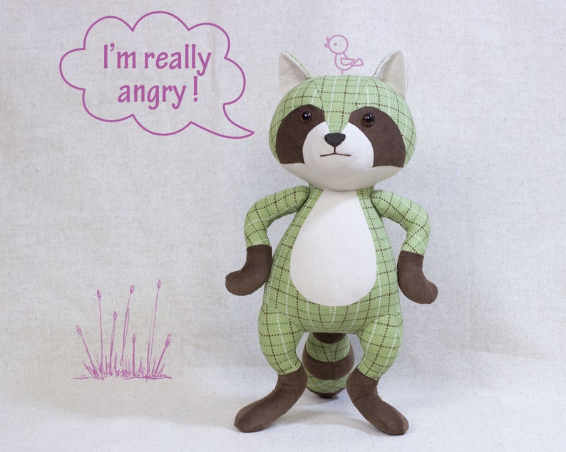 Puede incluir: Un juguete de peluche de mapache verde y marr&oacute;n con una barriga blanca y un peque&ntilde;o p&aacute;jaro en la cabeza. El mapache est&aacute; de pie con los brazos cruzados y tiene un globo de di&aacute;logo sobre su cabeza que dice "&iexcl;Estoy realmente enojado!"