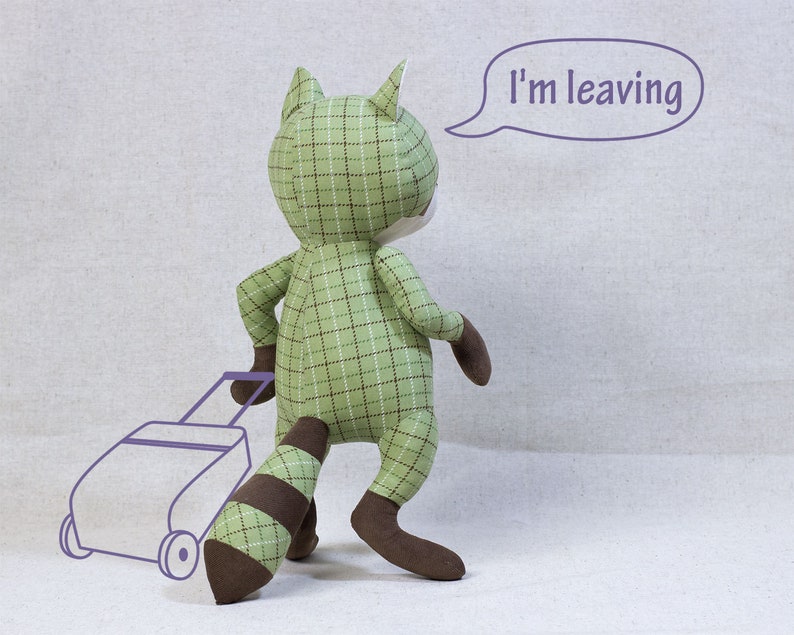 Puede incluir: Un juguete de peluche de mapache verde y marr&oacute;n con un patr&oacute;n de cuadros est&aacute; tirando de una peque&ntilde;a maleta con el texto "Me voy" en un globo de di&aacute;logo arriba.
