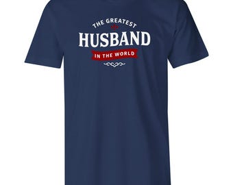 May include: Navy blue t-shirt with the text "THE GREATEST HUSBAND IN THE WORLD" in white and red. The text is arranged in a classic, decorative style. A perfect gift for a husband.