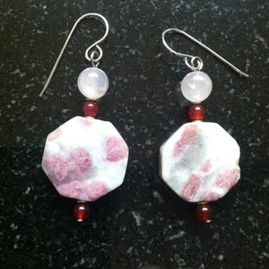 May include: A pair of silver earrings with pink and red gemstone beads. The earrings feature a large, octagonal pink and white gemstone with a silver wire loop.