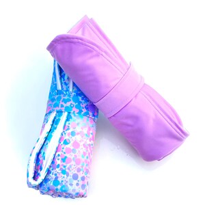 May include: Two rolled up towels, one with a pink solid color and the other with a white background and a colorful splatter pattern.