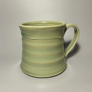 May include: A light green ceramic mug with a wide, rounded handle. The mug has a textured, striped design.