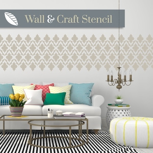 Puede incluir: Un sofá blanco con cojines de colores en un salón. La pared detrás del sofá tiene un patrón de plantilla beige con el texto "Wall & Craft Stencil".