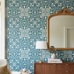 Könnte beinhalten: Türkis-weiße florale Tapete bedeckt die Wand. Ein goldgerahmter Spiegel hängt an der Wand. Ein Holzschrank mit Lampe und Dekoration befindet sich darunter. Die Tapete hat ein sich wiederholendes Muster aus stilisierten Blumen und Blättern.