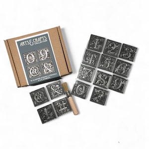 May include: A set of 15 silver metal stamps and stencils with a brush for applying ink. The stamps feature numbers 0-9 and symbols like "@" and "&" in a decorative font. The box reads "Arts & Crafts Collection".