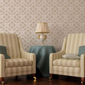 Op de afbeelding: Twee gestreepte fauteuils met kussens staan tegenover elkaar in een kamer met een behang met patroon. Een tafel met een blauw tafelkleed staat tussen de fauteuils en een lamp met een witte kap staat op de tafel.