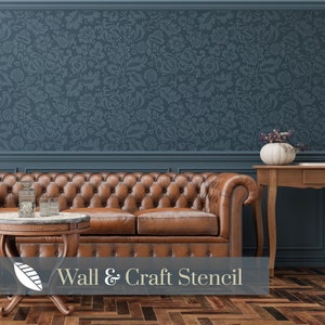 Puede incluir: Una plantilla de pared azul con un patrón floral. La plantilla se muestra en una pared detrás de un sofá de cuero marrón. El texto "Wall & Craft Stencil" se muestra debajo del sofá.