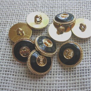 May include: A collection of round buttons featuring a glossy black center inlay surrounded by a textured gold-tone metal rim. Each button has a central gold-tone metal detail and a shank-style attachment on the back for sewing onto garments.