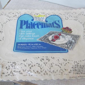 May include: A package of white lace placemats. The package has a blue label with the text "Placemats" and "Give your table settings that extra touch of elegance." Each mat measures 9 inches by 14 inches.