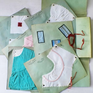 May include: A collection of vintage fabric swatches and garment patterns, including a teal gingham dress, white fabric samples, and pink fabric. The swatches are pinned to aged green paper, some with handwritten notes and red thread accents.