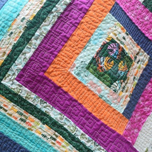 May include: A colorful quilt with a geometric pattern of squares and rectangles. The quilt is made of different fabrics with various patterns and colors, including turquoise, orange, purple, and green.