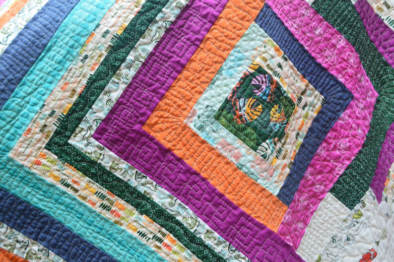 May include: A colorful quilt with a geometric pattern of squares and rectangles. The quilt is made of different fabrics with various patterns and colors, including turquoise, orange, purple, and green.