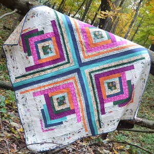 May include: A white quilt with a log cabin pattern in shades of pink, orange, teal, purple, and green. The quilt is made with a variety of fabrics and has a rustic, handmade look.